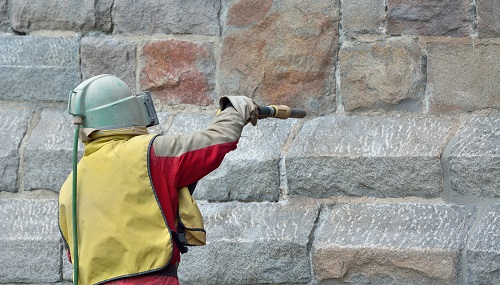 Worker sandblasting stone wall